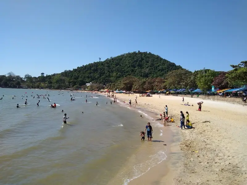 Families swimming and playing at Kep Beach below the forested hill