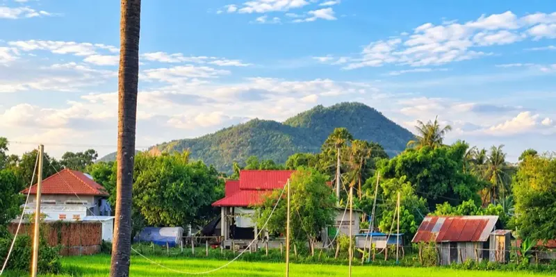 Village houses below a forested hill in the Kampot countryside