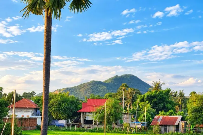 Village houses below a forested hill in the Kampot countryside